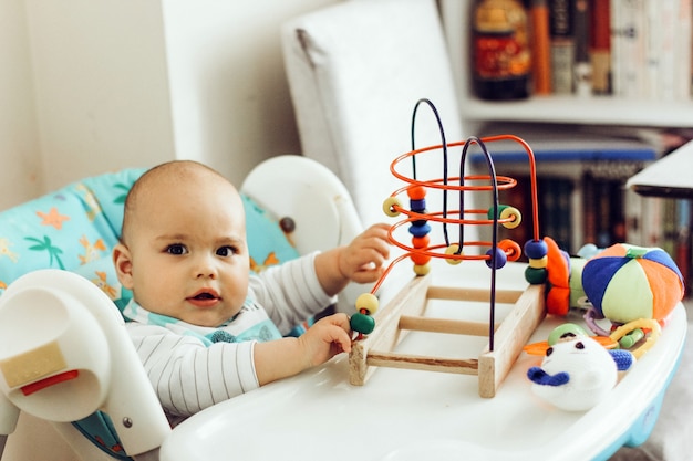 Petit garçon sérieux jouant des jouets dans une chaise haute à la maison