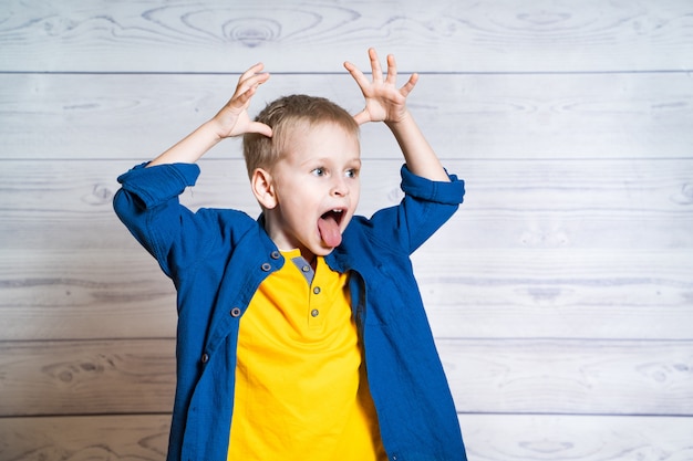 Petit garçon avec ses mains sur la tête montre sa langue. Un enfant drôle en t-shirt jaune et chemise bleue fait un visage stupide en regardant devant