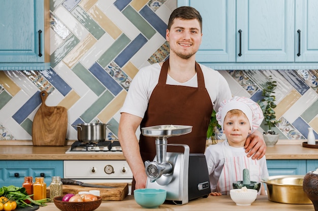 Un petit garçon et son beau père sourient en cuisinant des aliments dans la cuisine à la maison. Le concept de cuisine.
