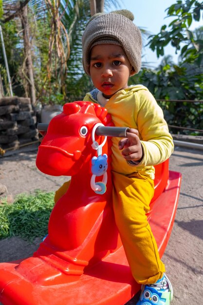 Petit garçon souriant assis sur un cheval jouet rouge le matin ensoleillé d'hiver Jouet cheval pour enfants d'âge préscolaire et tout-petits