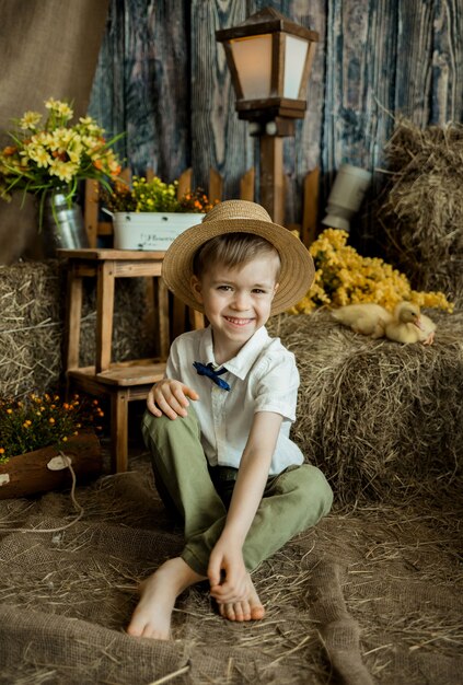 Petit garçon souriant dans un chapeau de paille est assis dans la paille avec des canetons. Fête de Pâques