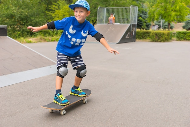 Petit garçon souriant filant sur une planche à roulettes dans un skate park alors qu'il profite de la liberté de ses vacances d'été