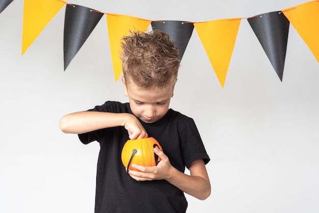 Un petit garçon souriant et heureux tient un panier d'Halloween en forme de citrouille et mange de la marmelade de bonbons