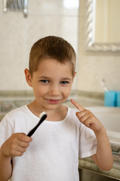 Un petit garçon en t-shirt blanc se brosse les dents Les dents de lait sont remplacées par des molaires