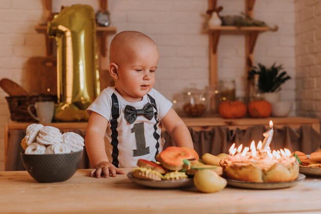 Un petit garçon en T-shirt avec le numéro un mange des sucreries maison saines dans la cuisine. guimauves, pain d'épice, tarte aux pommes, charlotte. boule de feuille d'or sous la forme d'un numéro un sur le fond