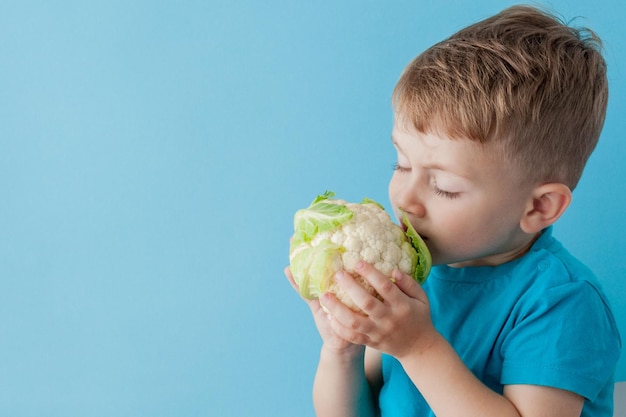 Petit garçon tenant le brocoli dans ses mains sur fond bleu alimentation et exercice pour un bon concept de santé