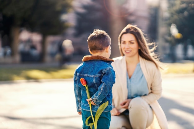 Un petit garçon tenant une fleur derrière son dos comme cadeau pour la mère le jour de la mère