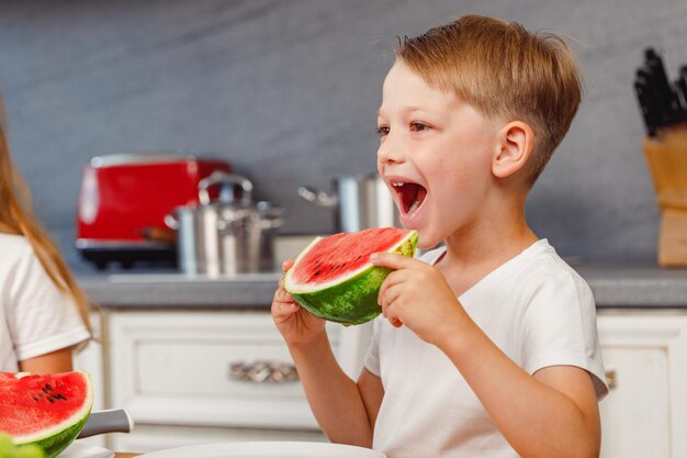 Petit garçon tenant un morceau de pastèque dans la cuisine