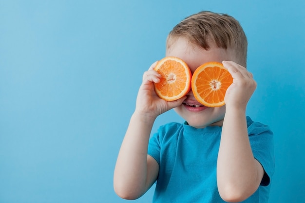 Petit garçon tenant une orange dans ses mains sur bleu