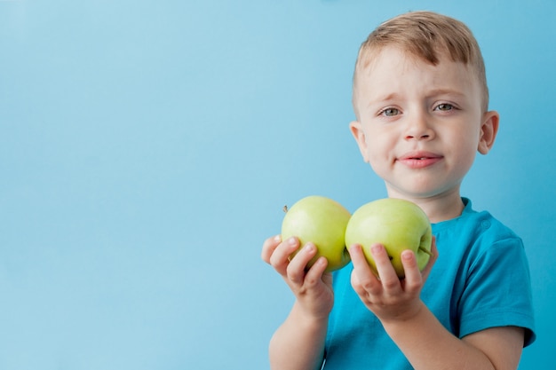 Petit garçon tenant une pomme dans ses mains sur fond bleu, régime alimentaire et exercice pour une bonne santé concept