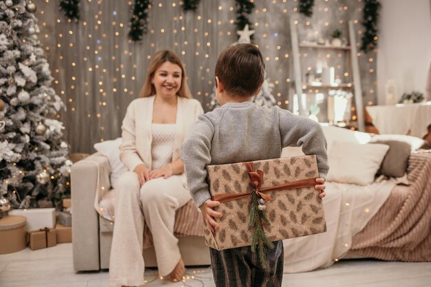 Le petit garçon tient un cadeau du Nouvel An pour maman dans la chambre