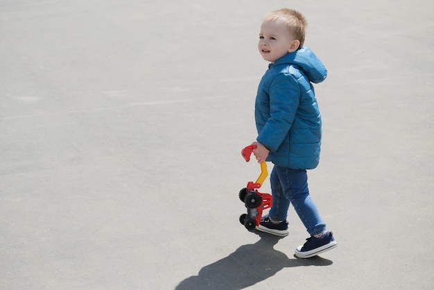Un petit garçon tient un camion jouet en plastique qui se promène à l'extérieur