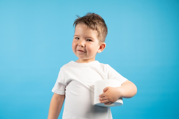 Un petit garçon tient doucement dans sa main un rouleau de papier toilette sur fond bleu Le concept d'achat de papier toilette Photo de haute qualité