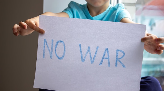 Un petit garçon tient un morceau de papier sur lequel est écrit non à la guerre