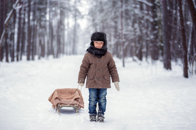 Petit garçon avec traîneau dans la forêt d'hiver