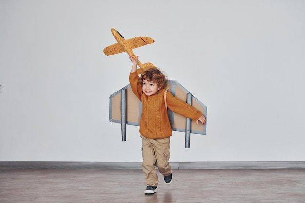 Petit garçon en uniforme de pilote rétro courant avec un avion jouet à l'intérieur