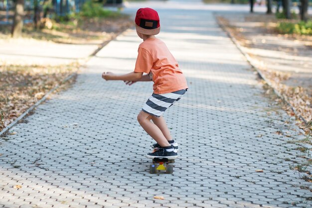 Petit garçon urbain avec une planche à roulettes penny. Kid patinage dans un parc d'été