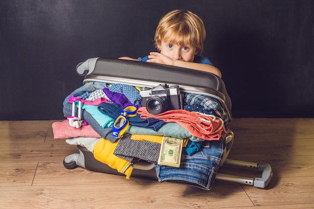 Petit garçon et valise de voyage. Enfant et bagages emballés pour des vacances pleins de vêtements, voyage d'enfant et de famille