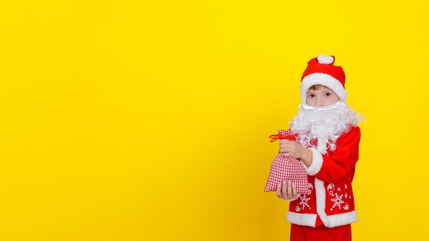 petit garçon en vêtements de Père Noël et barbe tient un petit sac avec des cadeaux du Nouvel An dans ses mains