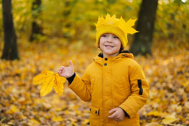 Un petit garçon vêtu d'un chapeau jaune et d'une veste se promène dans la forêt d'automne, l'enfant est actif dans la nature