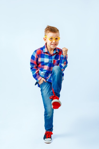 Petit garçon vêtu d'une chemise à carreaux colorée, jeans, gumshoes, lunettes en plastique s'amuser dans le studio