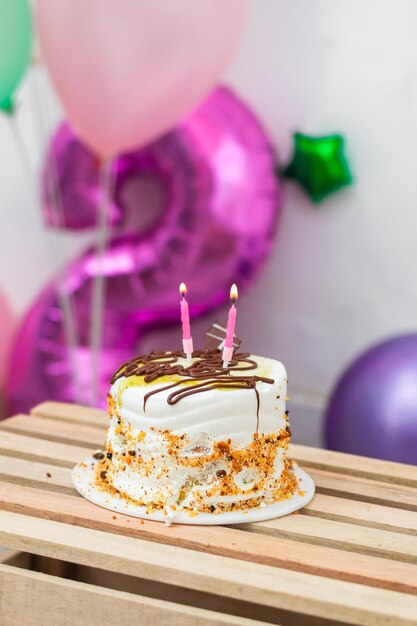 Photo petit gâteau d'anniversaire avec deux bougies allumées sur le dessus d'une table en bois avec des ballons