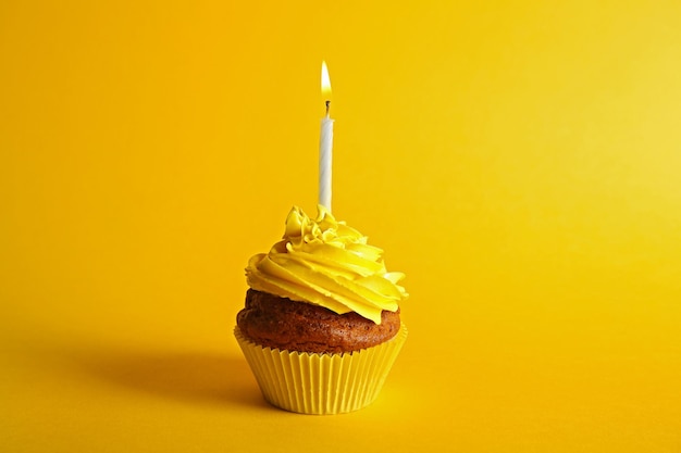 Petit gâteau savoureux frais avec bougie sur fond jaune