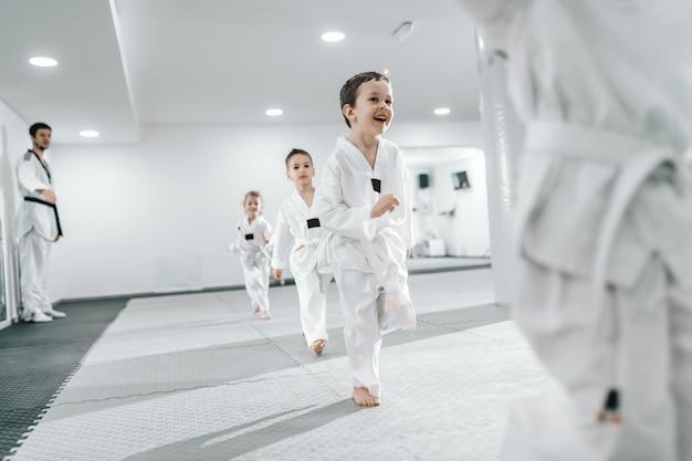 Petit groupe d'enfants s'entraînant au cours de taekwondo. Tous vêtus de doboks. Fond blanc.