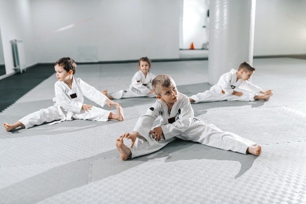 Petit groupe d'enfants sportifs caucasiens qui s'étirent et s'échauffent avant leur entraînement de taekwondo.