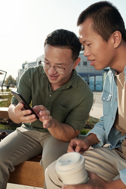 Petit groupe d'hommes d'affaires chinois discutant de quelque chose dans un smartphone