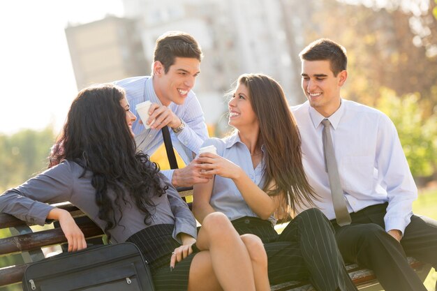 Un petit groupe de jeunes gens d'affaires pendant une pause-café, assis sur un banc de parc en profitant d'un café et d'une journée ensoleillée.