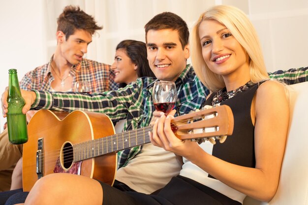 Photo un petit groupe de jeunes heureux traînent à la fête à la maison avec une guitare acoustique.