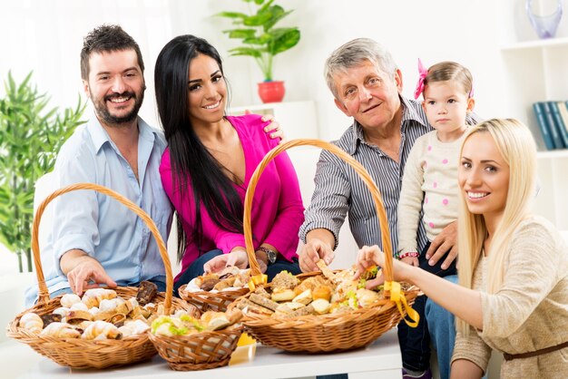 Un petit groupe de personnes, une famille heureuse dans leur maison mangeant des pâtisseries à partir de paniers tissés joliment décorés qui sont sur la table devant eux.