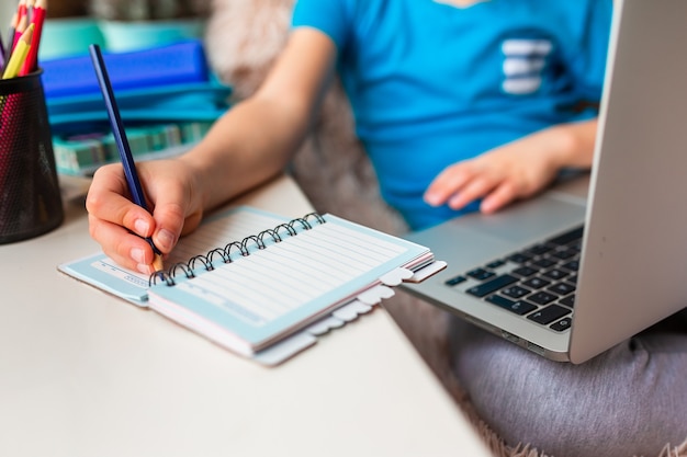 Petit jeune écolier travaillant à la maison avec un ordinateur portable et des notes de classe étudiant dans une classe virtuelle. Enseignement et apprentissage à distance, apprentissage en ligne, concept d'apprentissage en ligne pendant la quarantaine