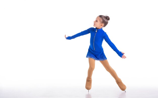 Un petit jeune patineur artistique posant en robe d'entraînement bleue sur la glace sur fond blanc