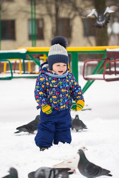 Le petit joli garçon nourrit les oiseaux dans le parc à neige d'hiver en plein air