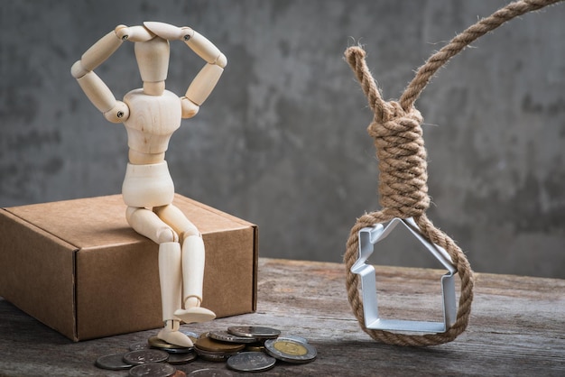 Petit mannequin en bois assis avec la maison et les pièces de monnaie du pendu