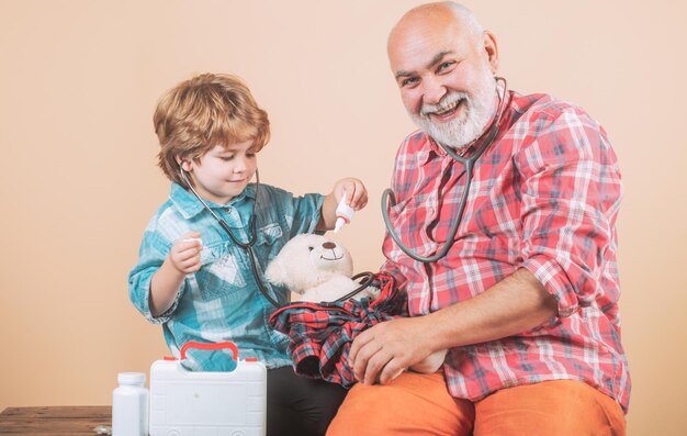 Petit médecin charmant petit garçon examinant une joue de son grand-père homme en écharpe colorée tricotée