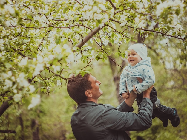 Petit mignon petit garçon avec son père marchant dans le parc du printemps en plein air. L'homme soulève son petit fils sur ses mains.