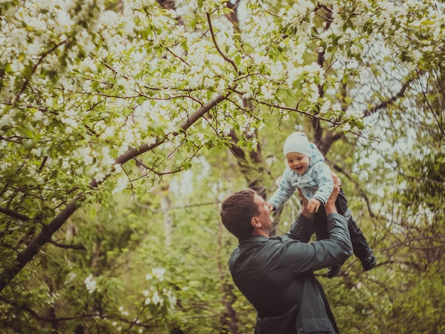 Petit mignon petit garçon avec son père marchant dans le parc du printemps en plein air. L'homme soulève son petit fils sur ses mains.