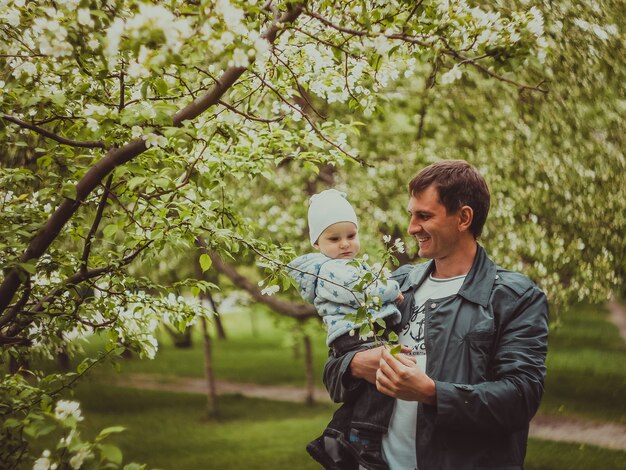 Petit mignon petit garçon avec son père marchant dans le parc du printemps en plein air. L'homme tient son petit fils sur les mains.