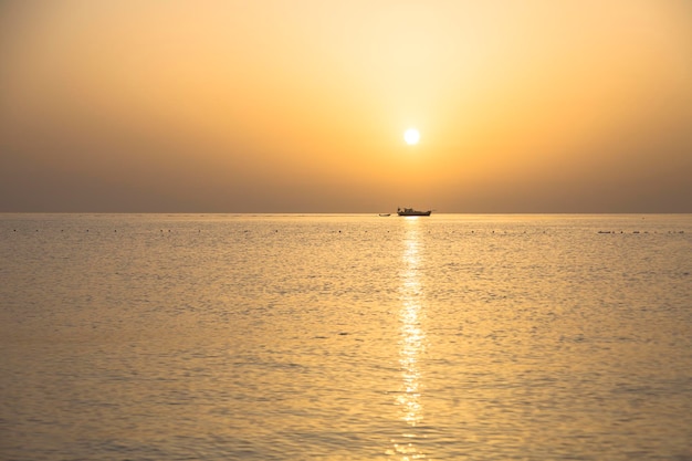 Petit navire avec bateau sous le disque orangé du coucher de soleil sur la mer pendant le coucher du soleil sur la mer Méditerranée