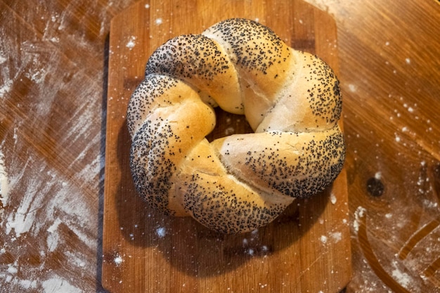 petit pain aux graines de pavot sur une planche de bois, la table est saupoudrée de farine vue de dessus