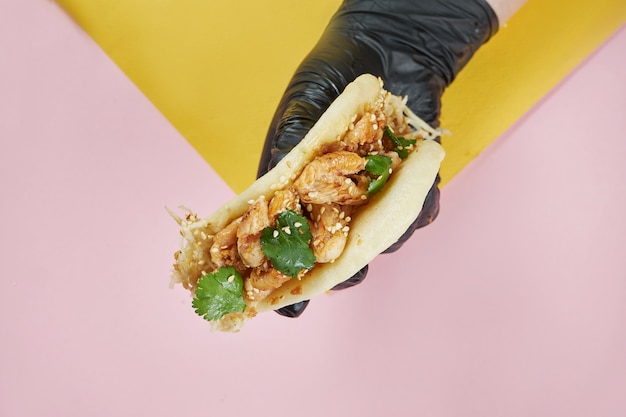 Petit Pain Bao Asiatique Traditionnel Avec Poulet Wok, Salade De Céleri Et Coriandre. Délicieuse Cuisine De Rue à La Main Sur Une Surface Colorée