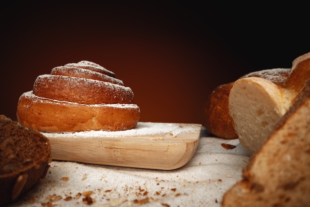 Petit pain à la cannelle frais avec du sucre en poudre sur planche de bois