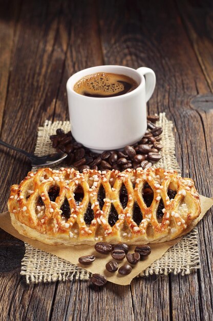 Petit pain sucré avec confiture et tasse de café sur une table en bois foncé