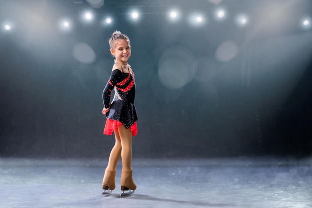 Un petit patineur monte sur des anneaux en robe rouge et noire sur une patinoire