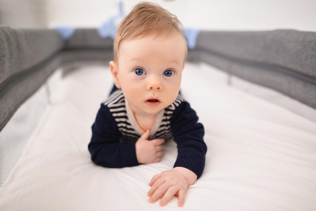 Petit petit bébé garçon de 5 mois qui pleure allongé sur le lit en essayant de ramper