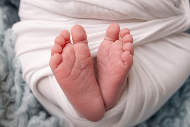 Le petit pied d'un nouveau-né. Pieds doux d'un nouveau-né dans une couverture blanche et sur fond bleu. Gros plan sur les orteils, les talons et les pieds d'un nouveau-né. Macro photographie en studio. Le bonheur de la femme.