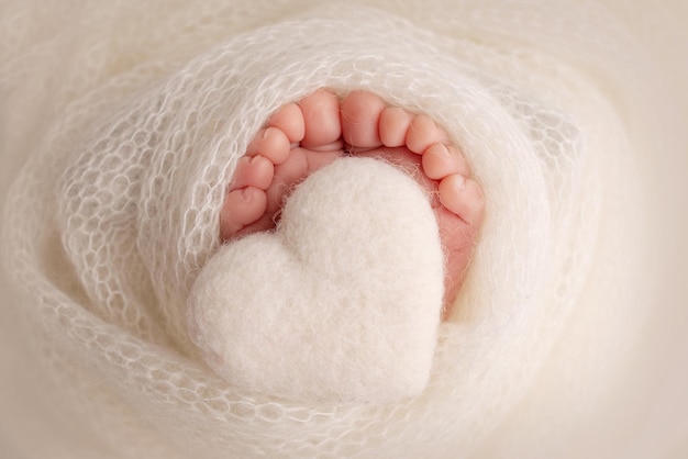 Le petit pied d'un nouveau-né Pieds doux d'un nouveau-né dans une couverture en laine blanche Gros plan sur les orteils, les talons et les pieds d'un nouveau-né Coeur blanc tricoté dans les jambes d'un bébé Macro photographie